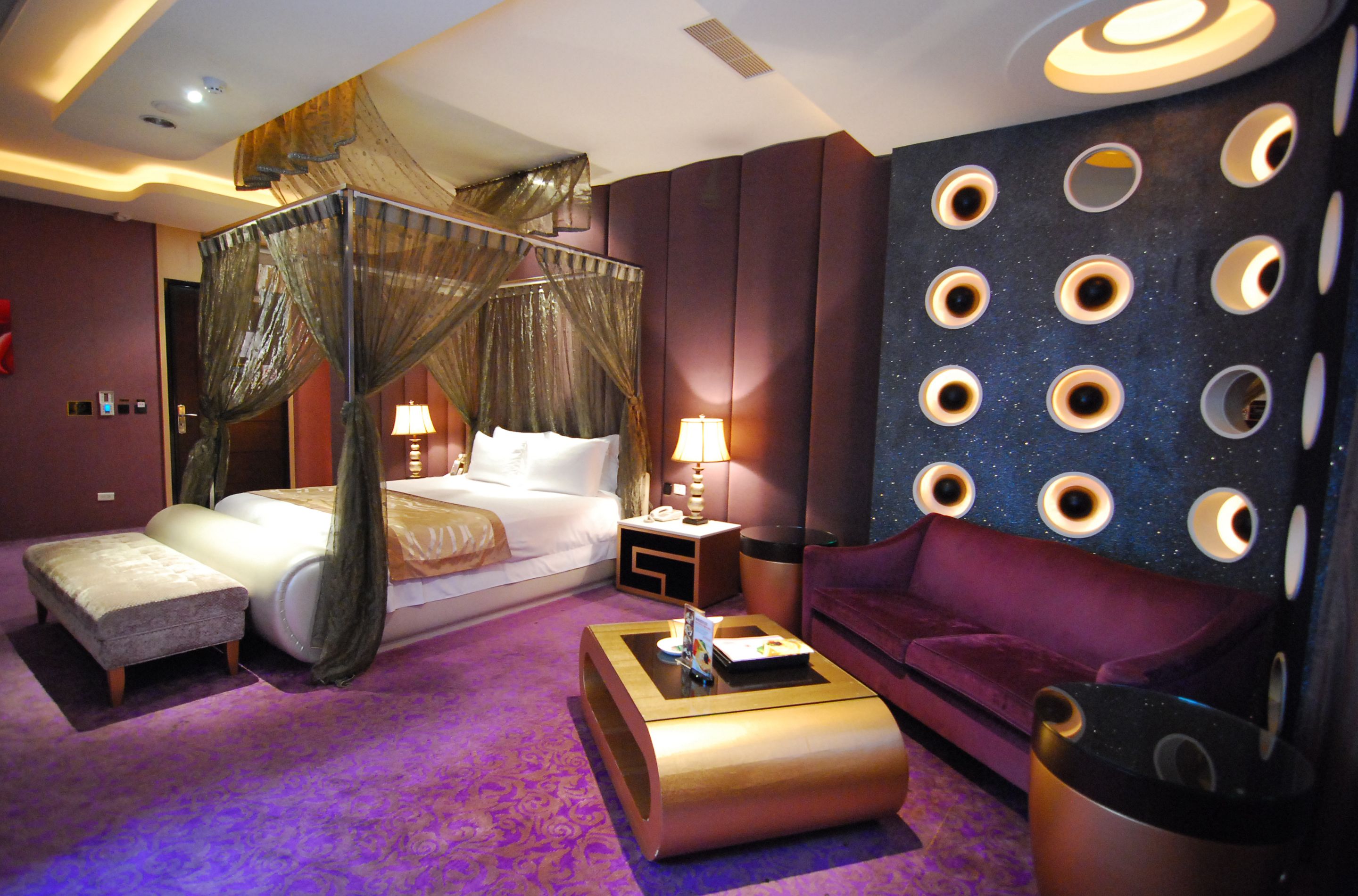 A hotel room with a four-poster bed, a sofa, a coffee table, and a wall with circular cutouts.