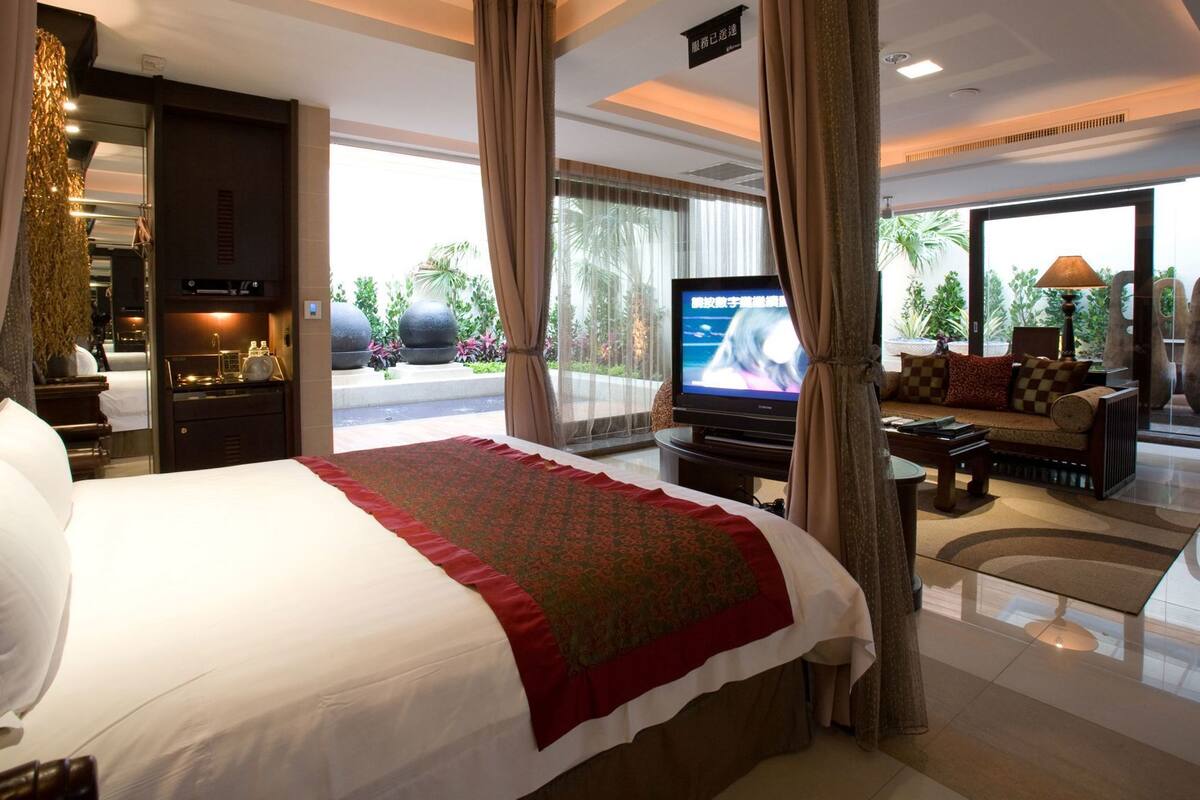 A hotel room with a large bed, a television, a sofa, and a view of the outdoors.