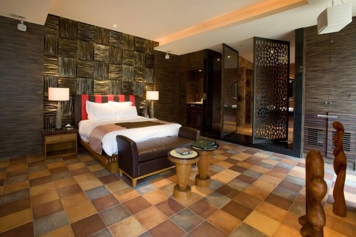 A modern hotel room with a large bed, a sofa, a small round table, and a decorative wall panel.