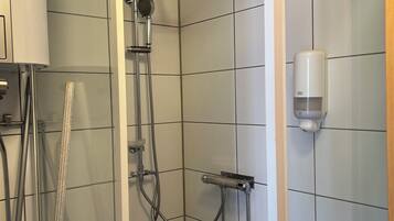 A shower with a glass door, a handheld showerhead, and a wall-mounted soap dispenser.