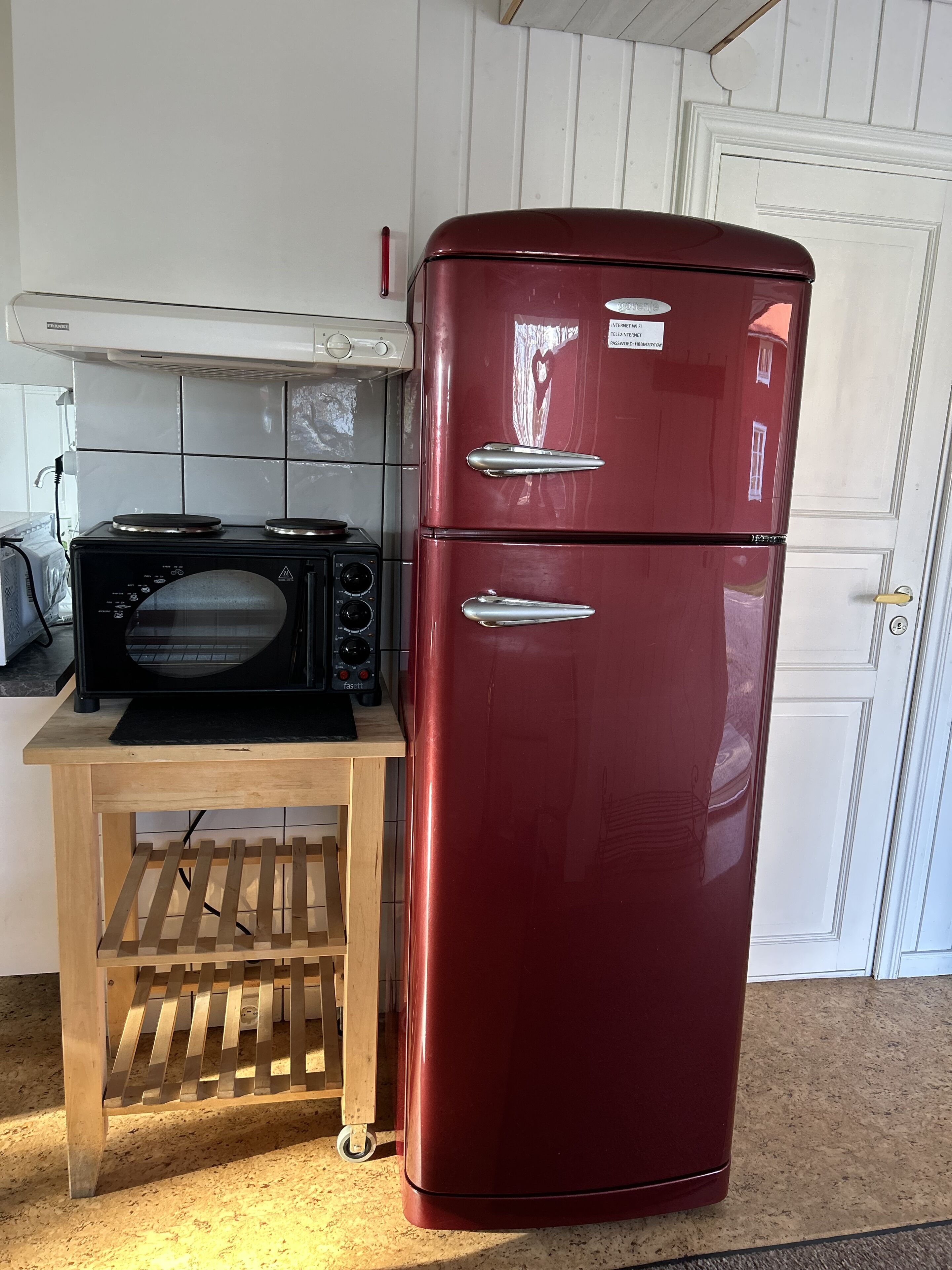 Eine Küche mit einem roten Kühlschrank, einer schwarzen Mikrowelle und einem Holztisch mit einem Metallregal.