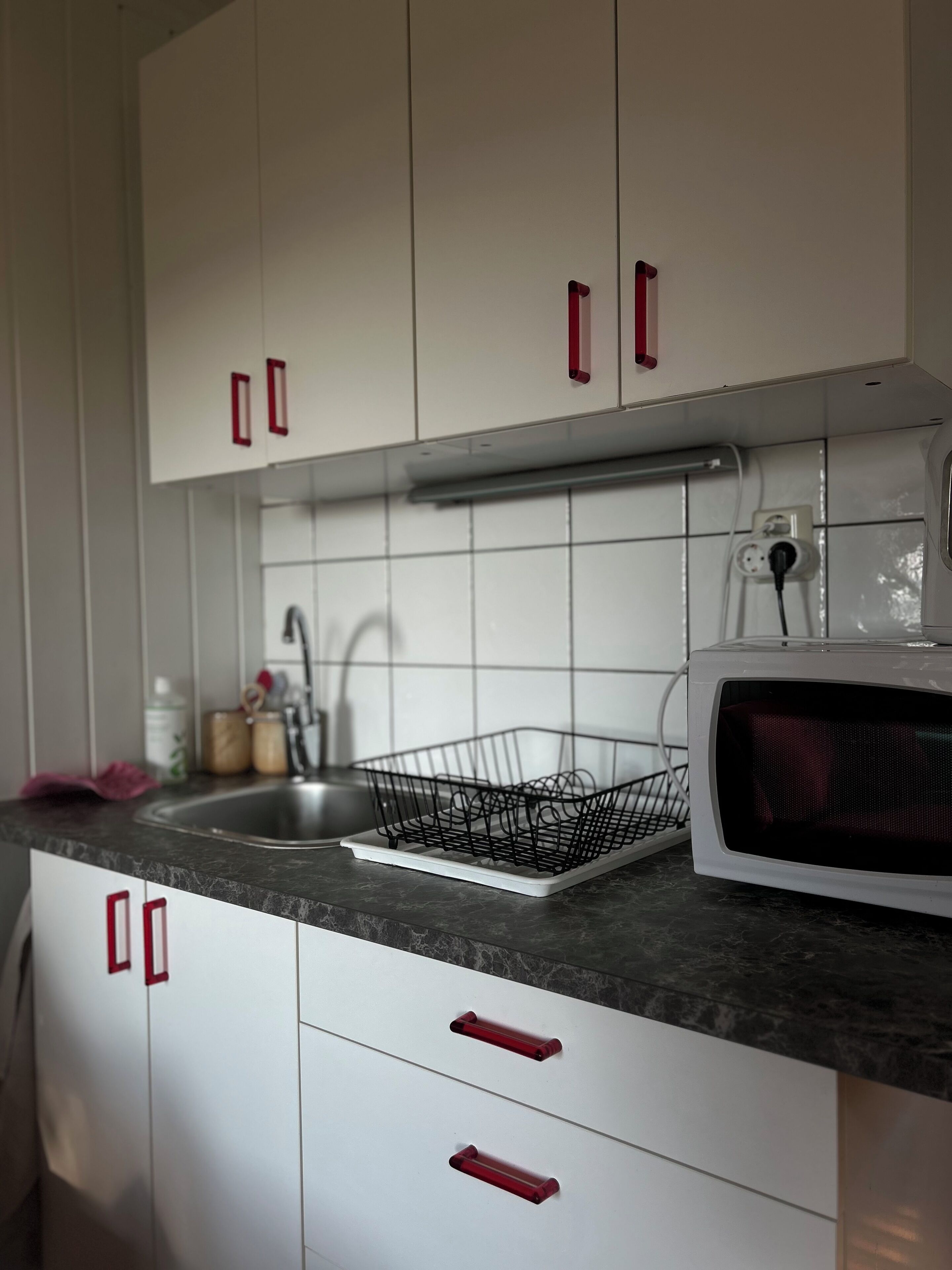 A kitchen with white cabinets, a sink, a microwave, and a black wire dish rack.