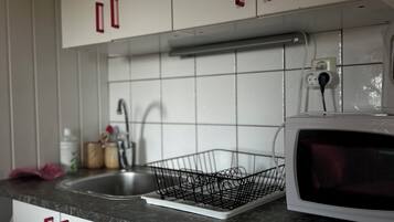 A kitchen with white cabinets, a sink, a microwave, and a black wire dish rack.