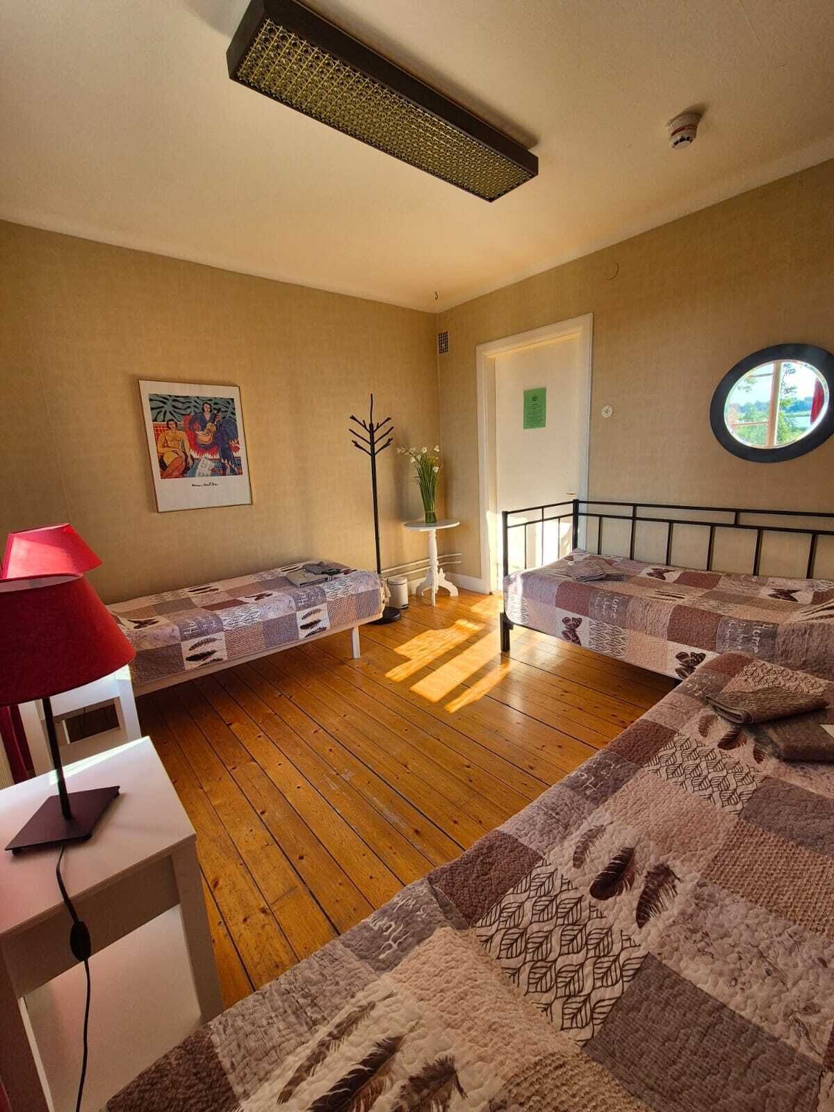Una habitación con dos camas, un escritorio con lámpara, un cuadro en la pared y una ventana.
