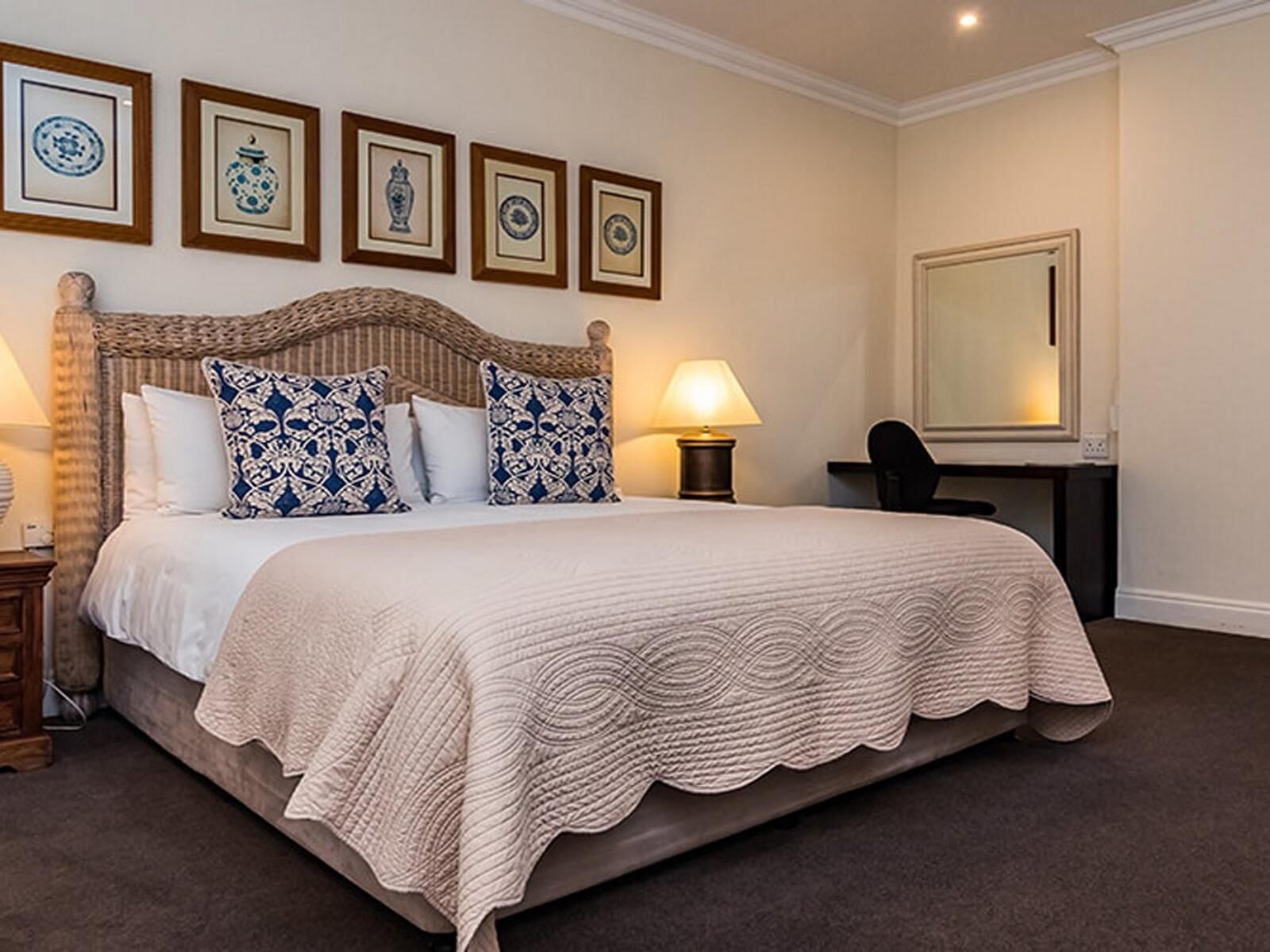A neatly made bed with a patterned headboard, a bedside lamp, and a desk with a chair.