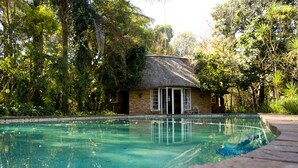 Una piscina con una estructura de techo de paja al fondo.