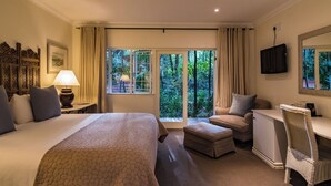 Habitación de hotel con una cama grande, un escritorio, una silla y vistas a la vegetación por las ventanas.