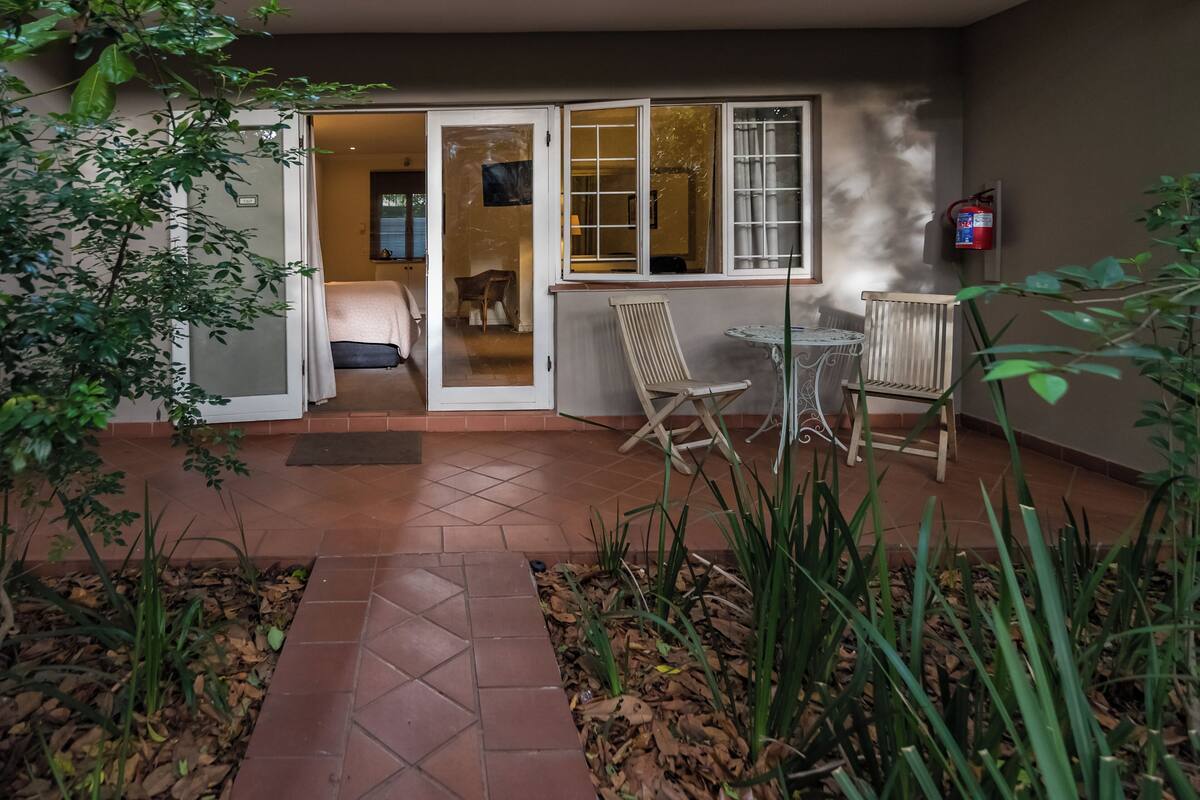 A patio area with a sliding glass door leading to a bedroom, a small table with chairs, and a fire extinguisher mounted on the wall.