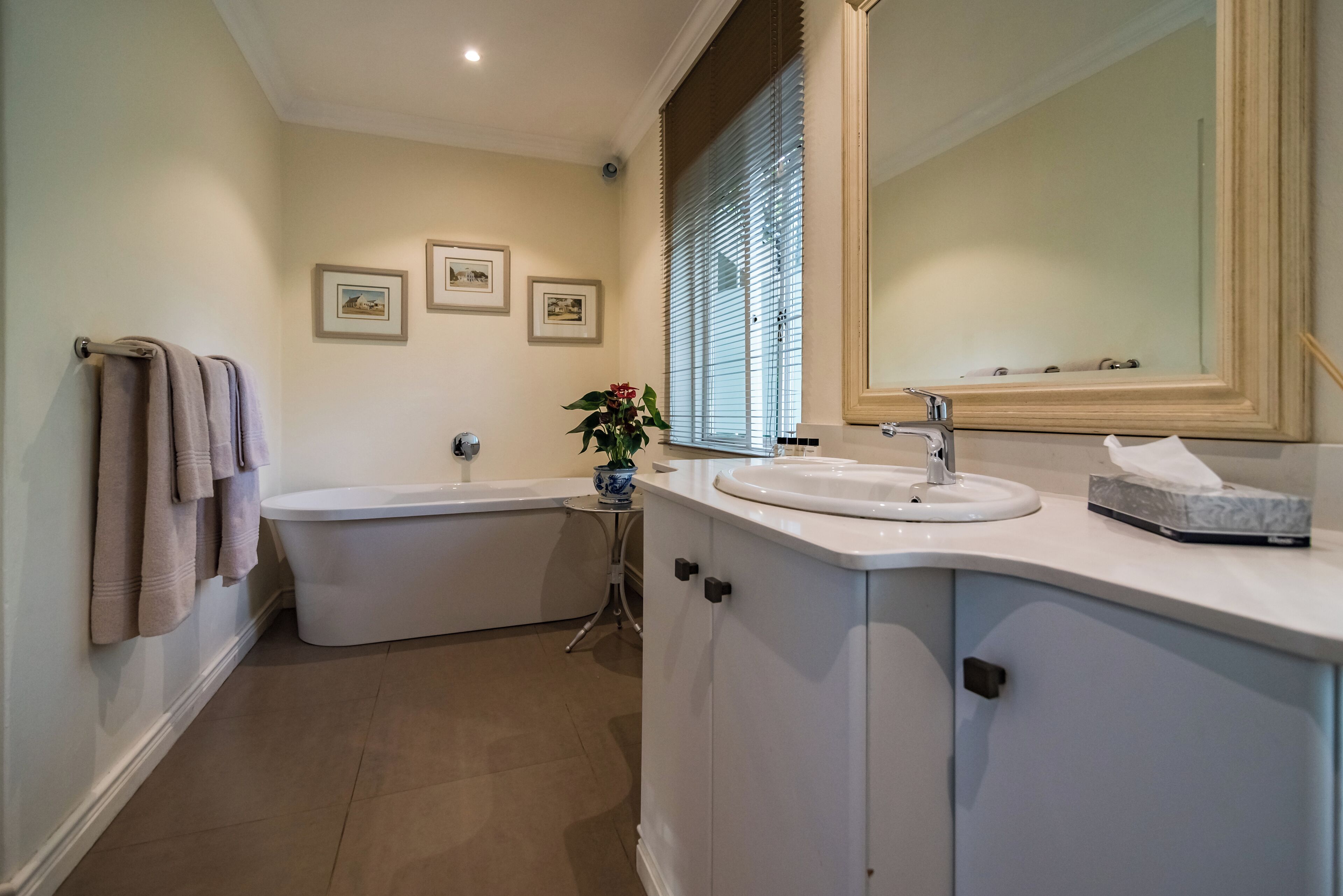 A bathroom with a bathtub, a sink, a mirror, and framed pictures on the wall.
