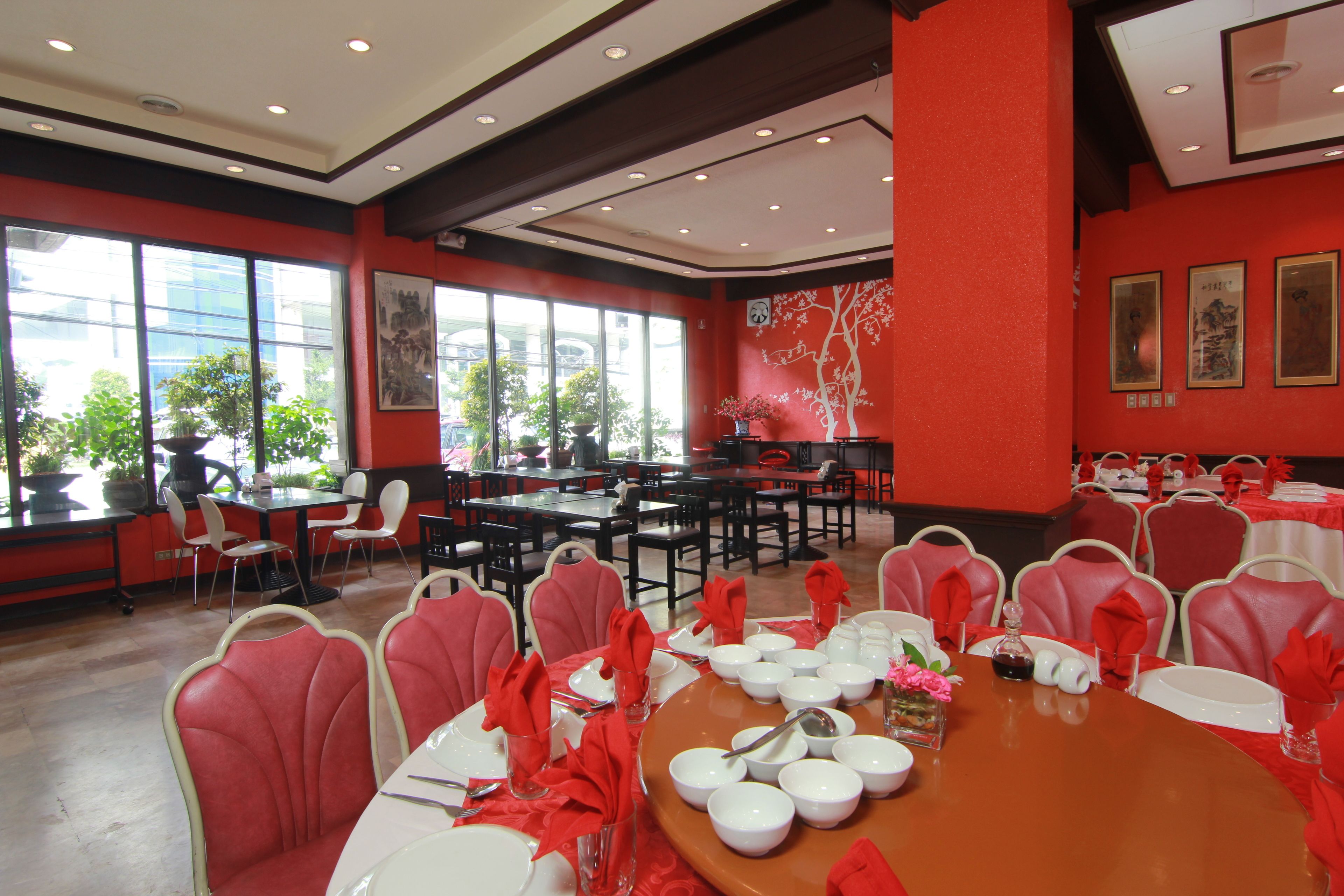 Un comedor con paredes rojas, varias mesas dispuestas para comer y sillas con servilletas rojas.