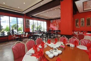A dining area with red walls, multiple tables set for dining, and chairs with red napkins.