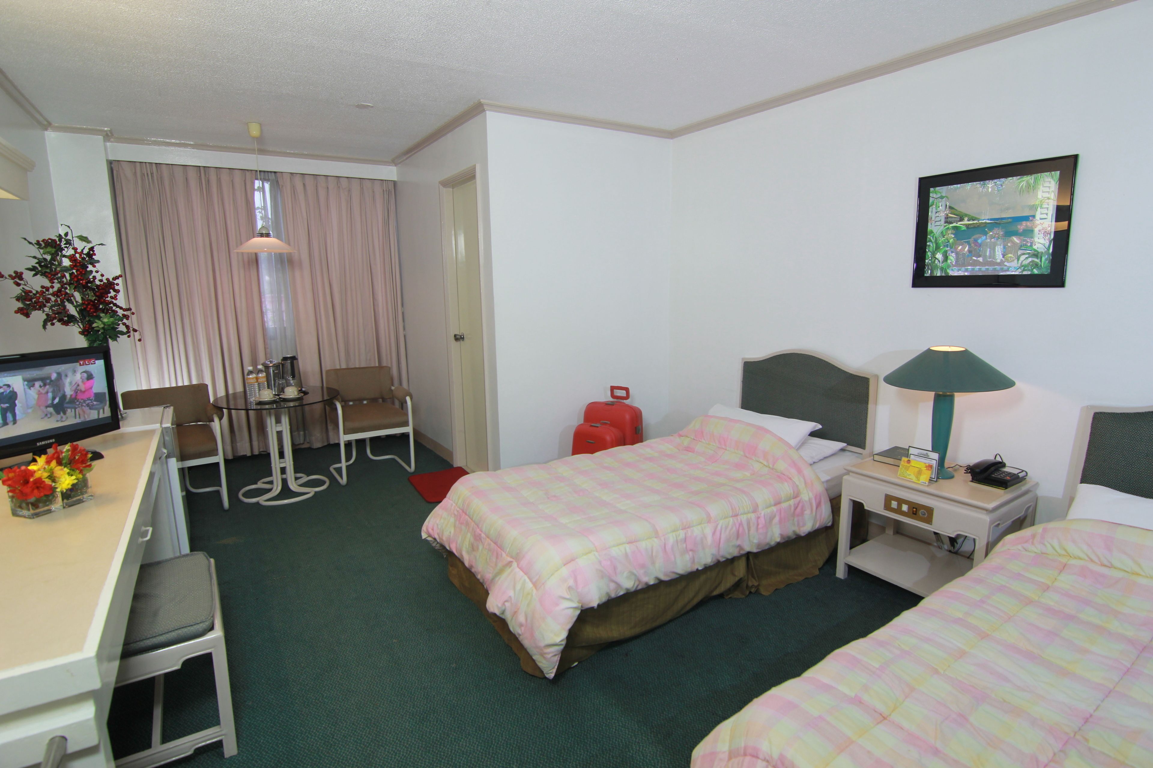 Habitación de hotel con dos camas, un escritorio con computadora, una silla, una mesa, una lámpara y un televisor.