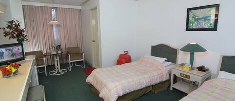 Habitación de hotel con dos camas, un escritorio con computadora, una silla, una mesa, una lámpara y un televisor.