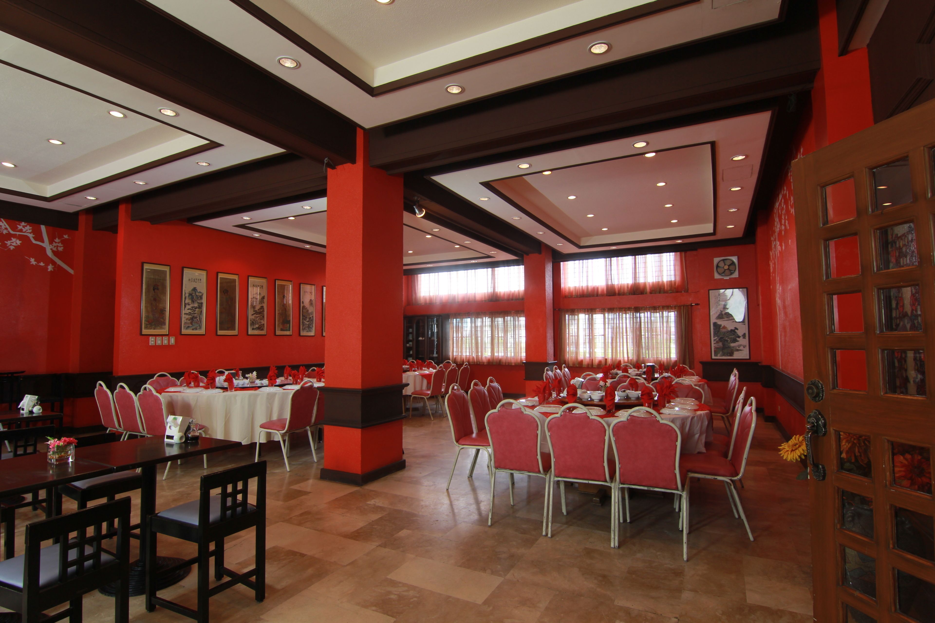 A spacious dining area with red walls, multiple tables, and chairs.