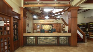 A reception desk with a sign reading "Hotel Supreme," wooden paneling, a staircase, and a tiled floor. - Hotel Supreme (Baguio)