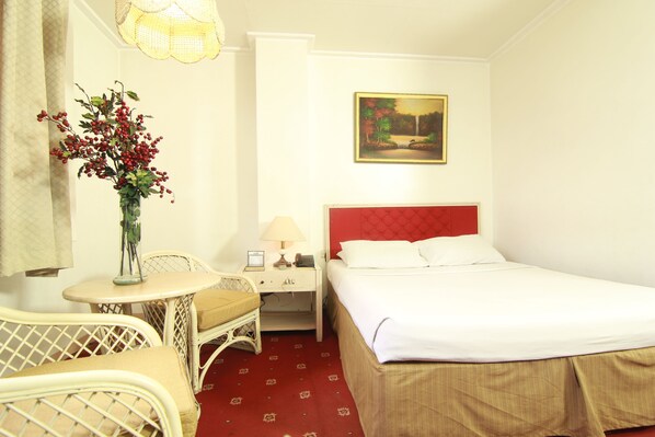 Habitación de hotel con cama, una mesita de noche con lámpara, una silla y un jarrón con bayas rojas.