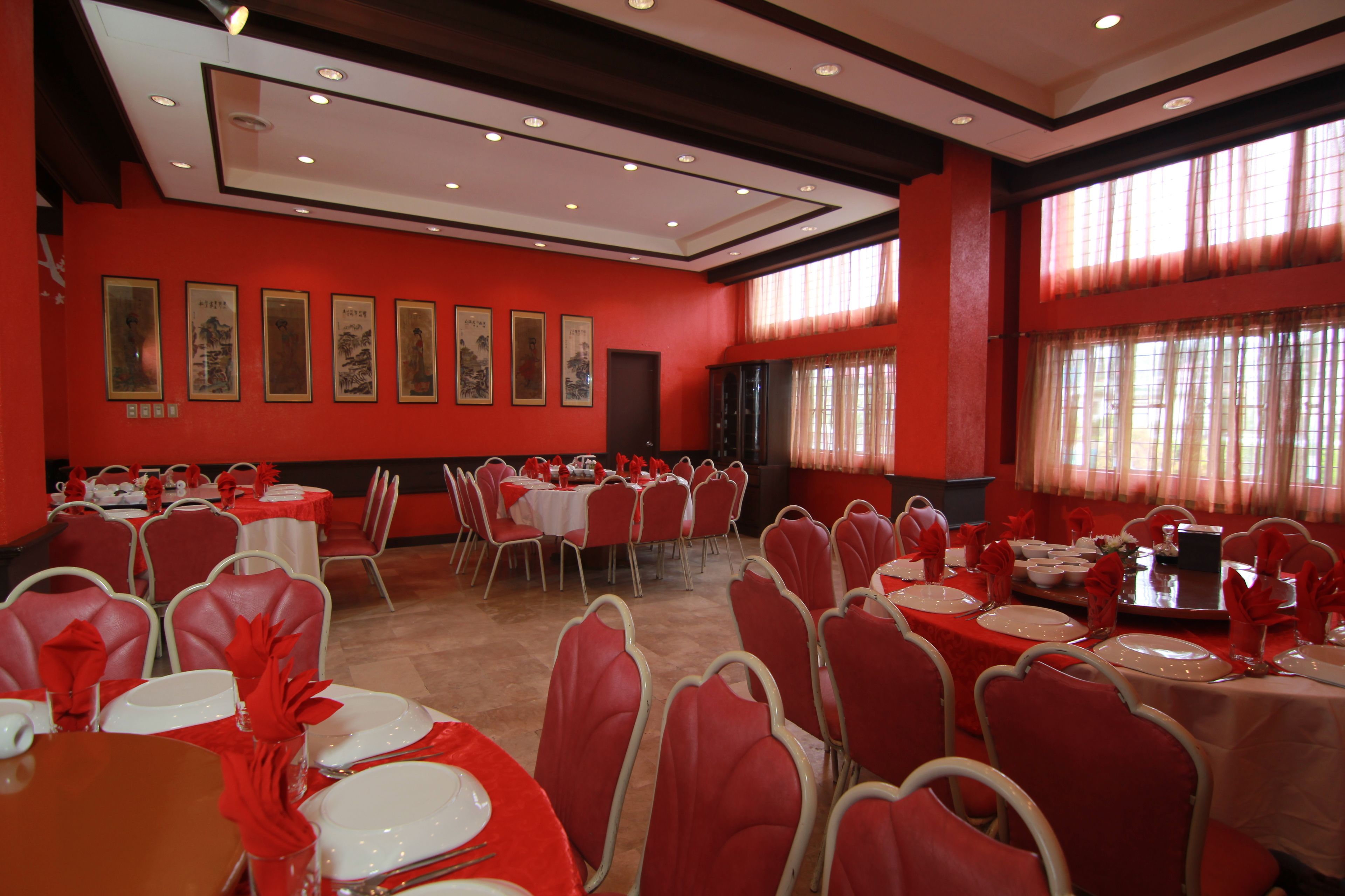 A banquet hall with red walls, multiple round tables set for dining, and framed pictures on the walls.