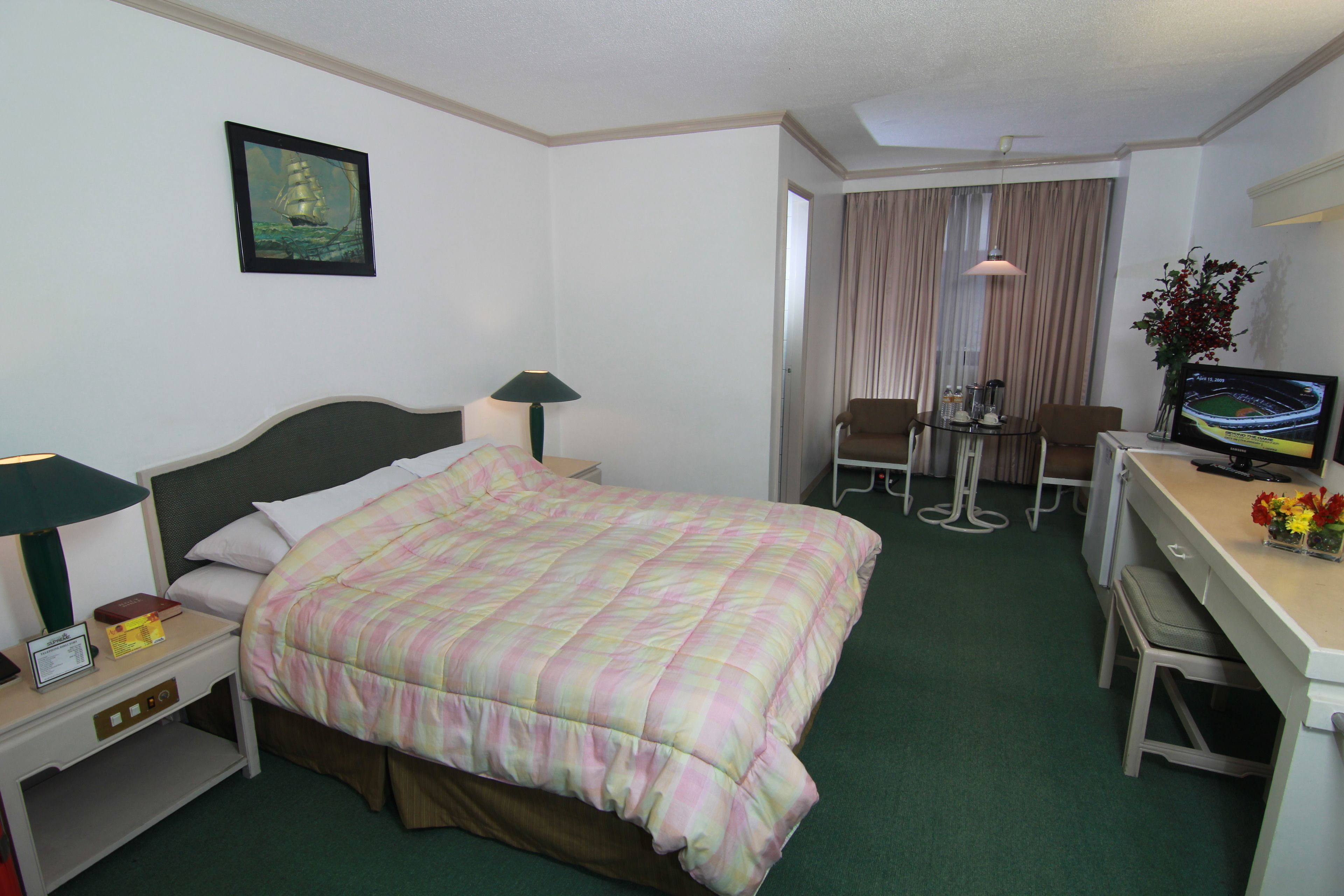 A hotel room with a bed, a desk with a computer and a chair, a TV, and a painting on the wall.