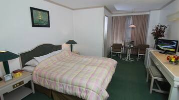 Habitación de hotel con cama, escritorio con computadora y silla, televisor y un cuadro en la pared.