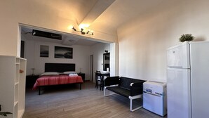 Ein kleines Hotelzimmer mit einem Bett, einem Schreibtisch, einem Stuhl, einem Kühlschrank und einem Tisch.