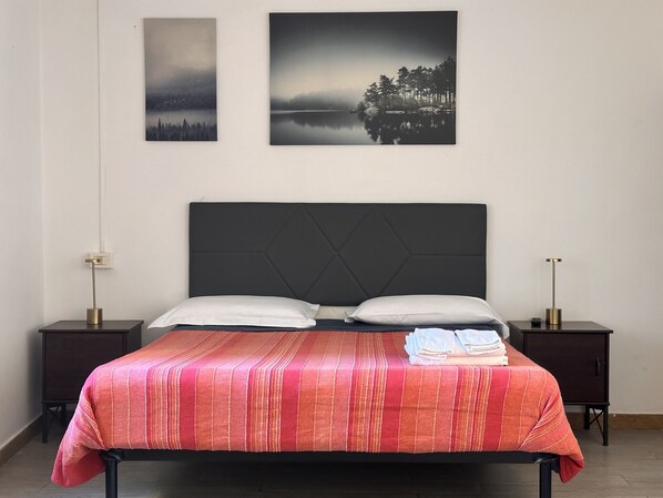 A bed with a red striped bedspread, two white pillows, and a folded towel on the side. There are two bedside tables with lamps, and two framed pictures on the wall above the bed. - Locanda San Lorenzo (Florence)
