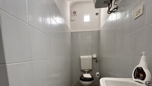 Ein Badezimmer mit grauen Fliesenwänden, Holzboden, Waschbecken in Weiß und Toilette mit schwarzem Deckel.