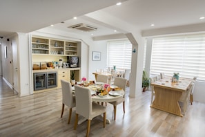 Una cocina moderna con estantes integrados, un comedor con mesa y sillas de madera, y un amplio ventanal con persianas.