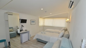 Una habitación de hotel moderna con cama, escritorio, silla, refrigerador pequeño y televisor.