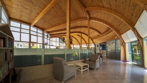 Une pièce spacieuse avec un haut plafond en bois, de grandes fenêtres et un coin salon comprenant des canapés et une table.