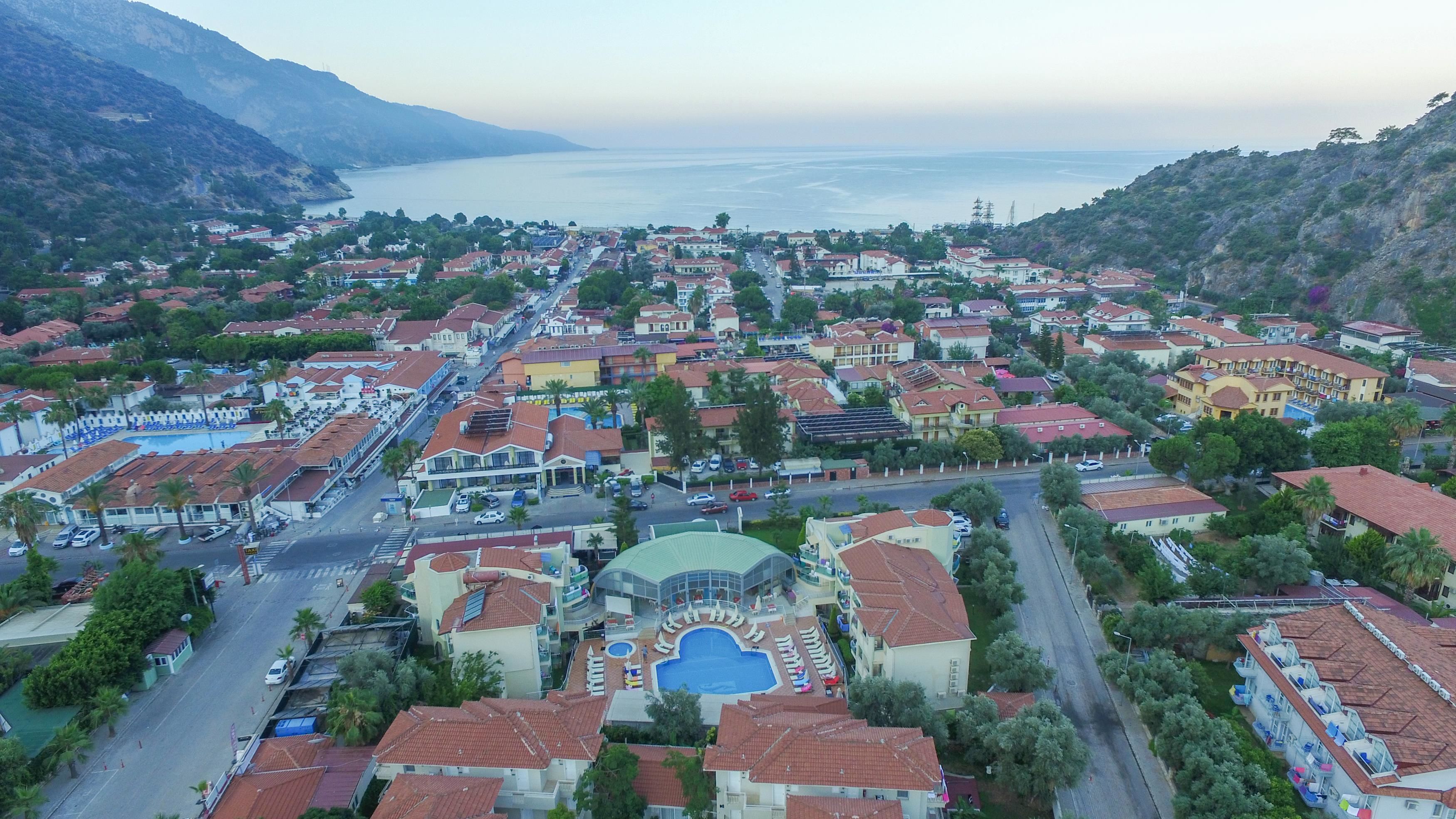 An aerial view of a coastal town with a central swimming pool surrounded by buildings with red-tiled roofs.