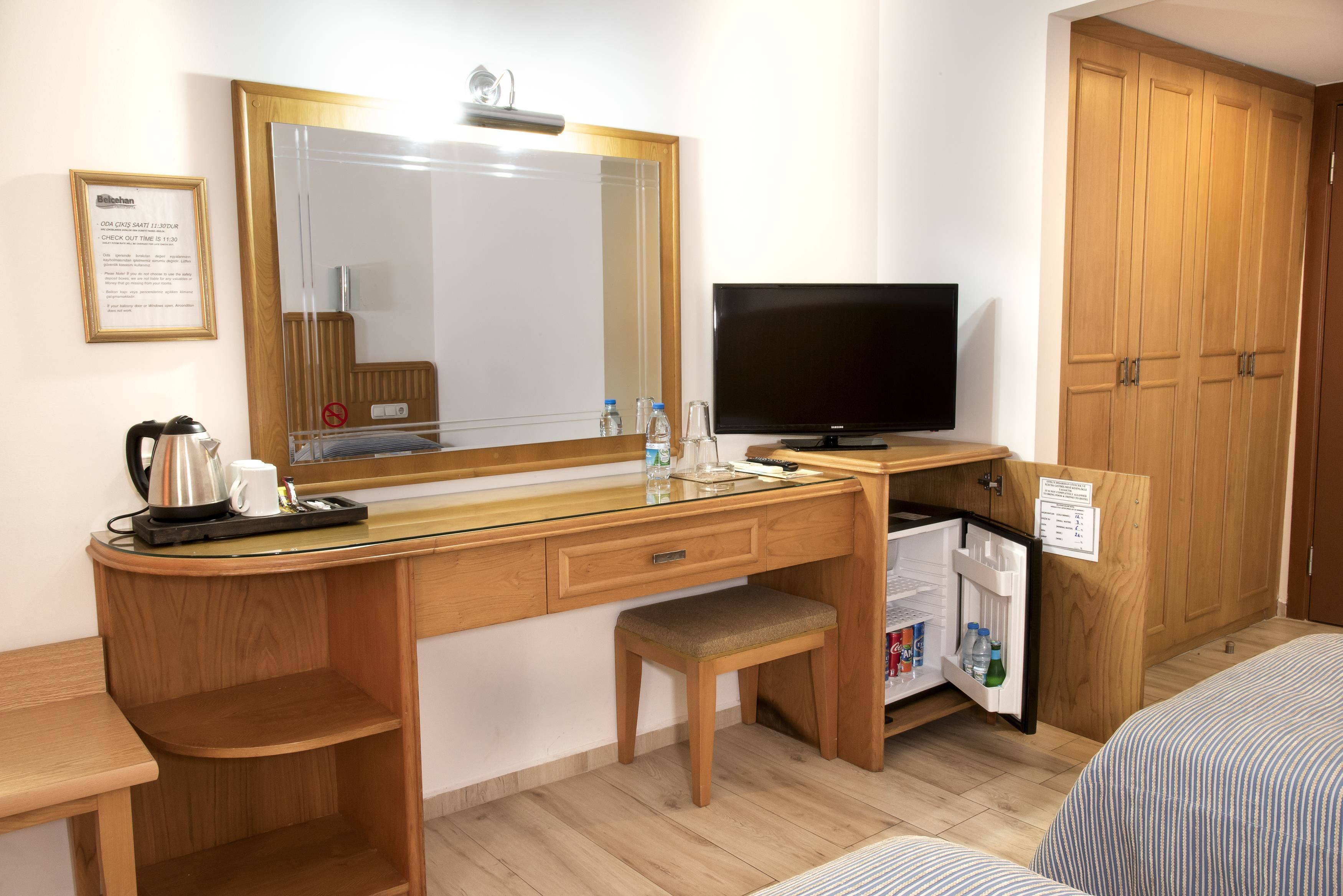 A hotel room with a wooden desk, a television, a mini-fridge, and a bed with striped bedding.
