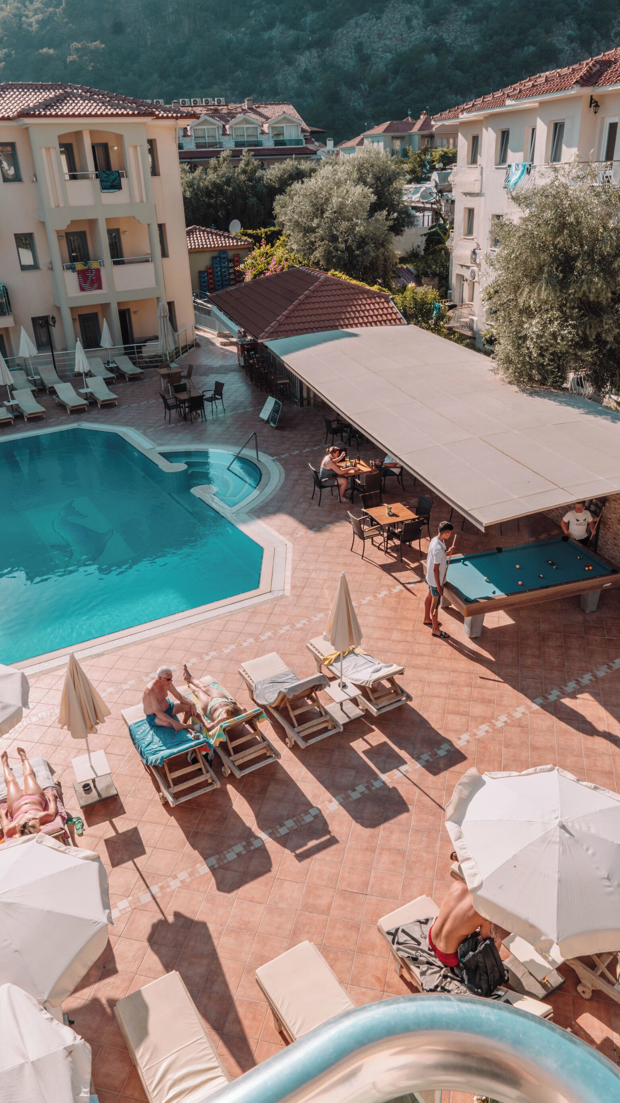 A pool area with lounge chairs, a pool table, and a covered seating area.