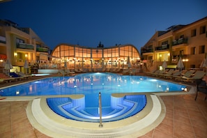 A swimming pool with sun loungers and a building with balconies in the background. - Belcehan Hotel (Fethiye)