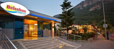 The exterior of the Belcehan Deluxe Hotel with a staircase leading to the entrance, surrounded by a mountainous landscape.