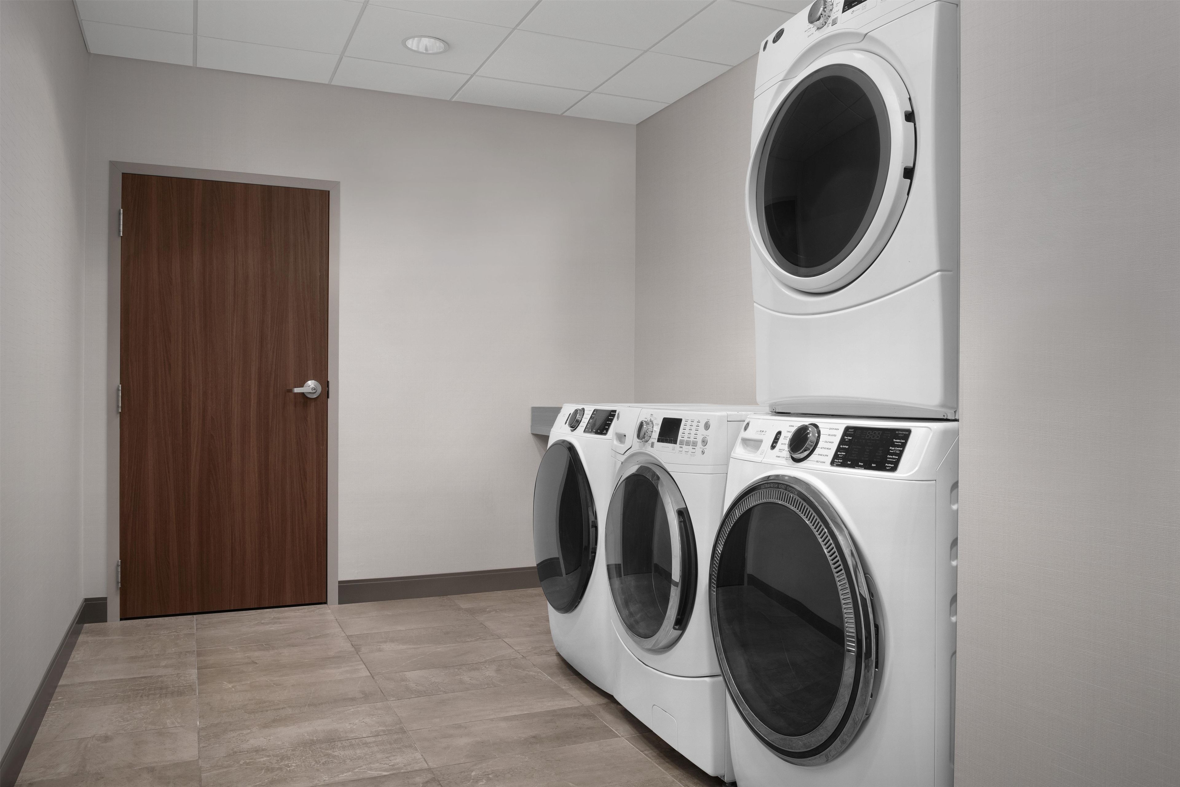 A laundry room with a wooden door, two stacked front-loading washing machines, and a tiled floor.