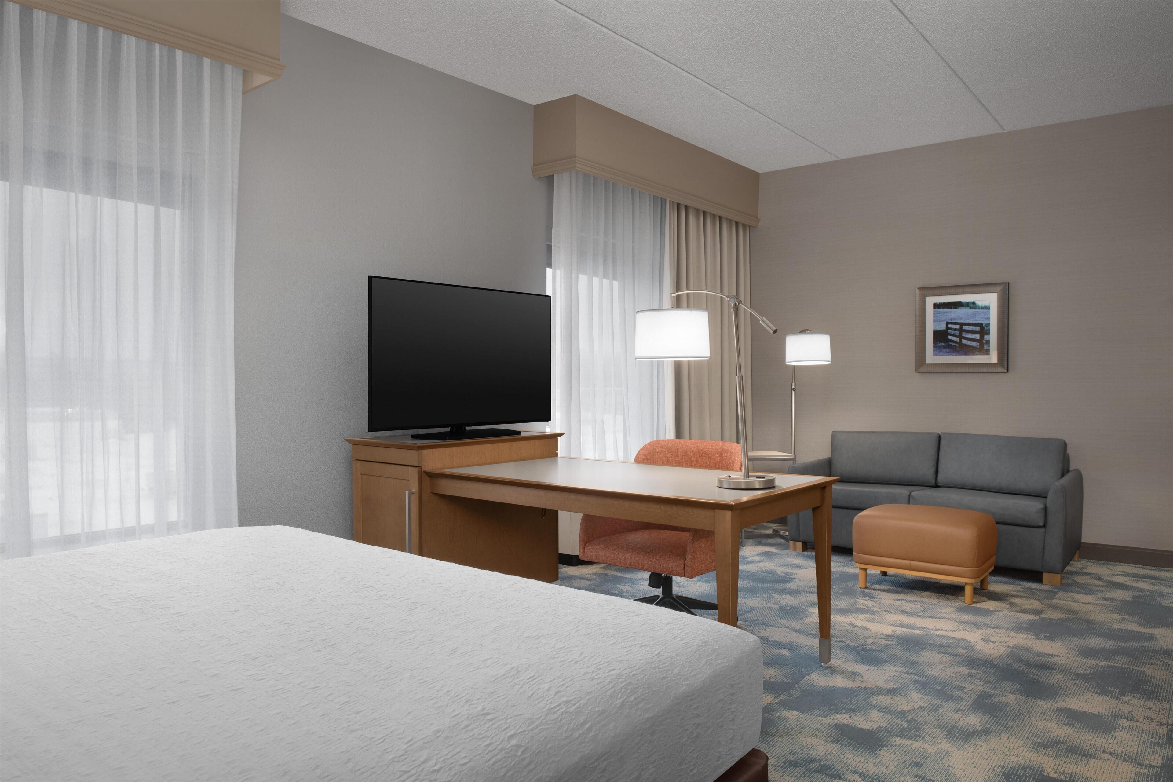 Ett hotellrum med en säng, ett skrivbord med en tv, en soffa och en lampa.