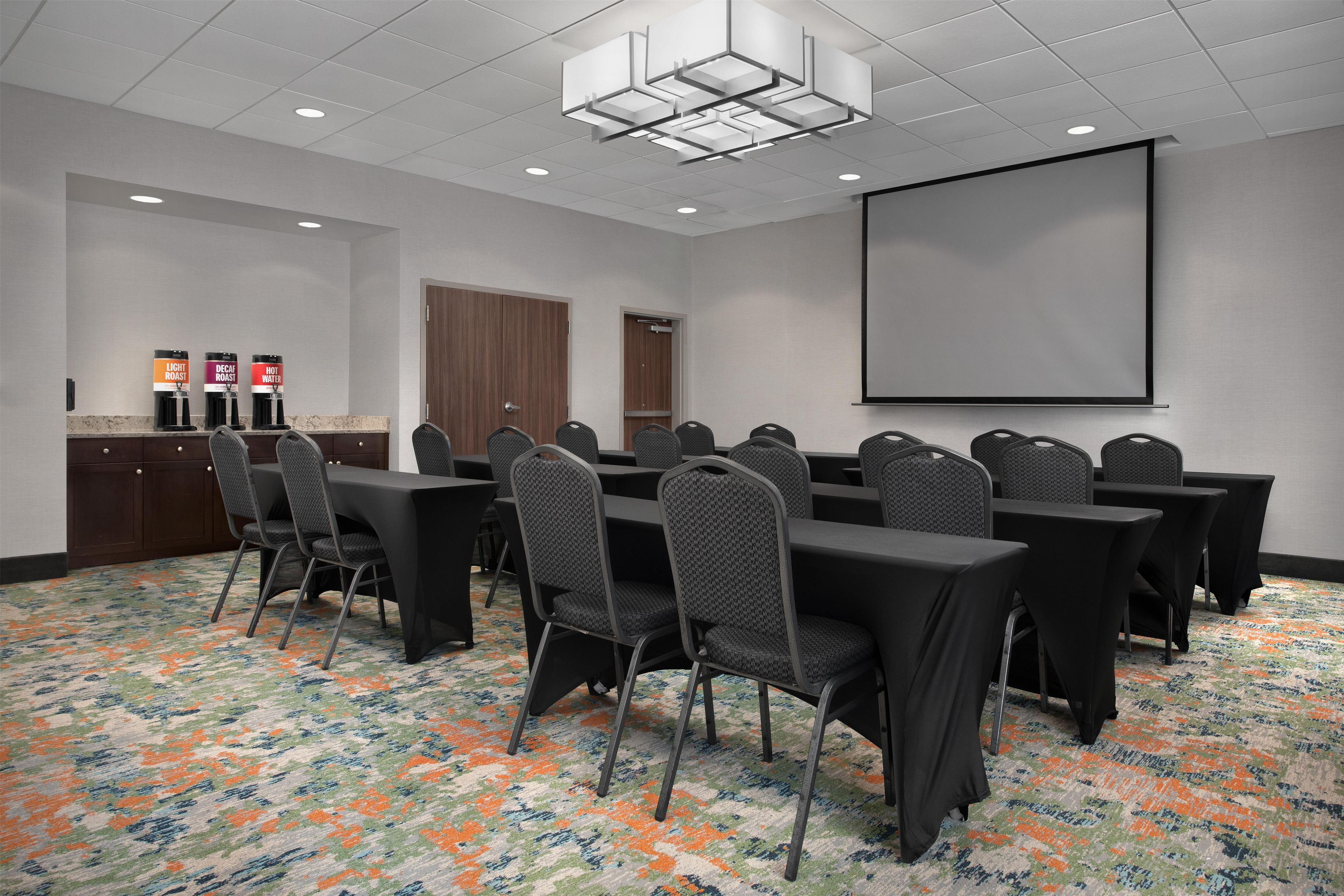 A conference room with a large table, chairs, a projector screen, and a coffee station.