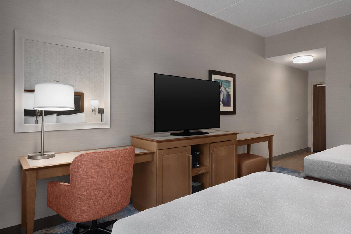 A hotel room with a bed, a desk with a chair, a television, and a framed picture on the wall.