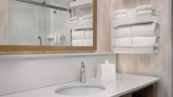 A modern bathroom with a large mirror, a sink, and neatly stacked towels on a shelf.