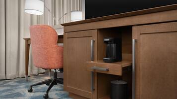 A hotel room with a wooden desk, an orange office chair, a coffee maker, and a trash can.