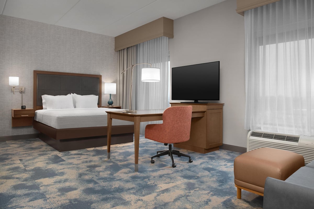 A hotel room with a bed, desk, chair, TV, and a window with curtains.