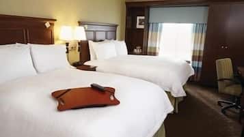 A hotel room with two beds, a desk, a chair, and a window with curtains.