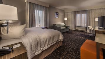 A hotel room with a large bed, a desk with a chair, a television, and a window with curtains.