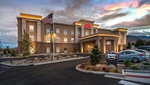 A Hampton Inn & Suites hotel with a flag in front, a parking lot, and a mountainous backdrop. - Hampton Inn & Suites Reno West (Reno)