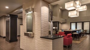 A modern lobby with a reception desk, red seating, and a decorative wall. - Hampton Inn & Suites Reno West (Reno)