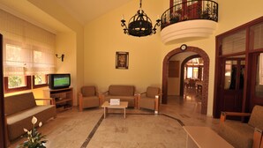 Amplia sala de estar con televisor, asientos cómodos, una araña y vista al comedor.