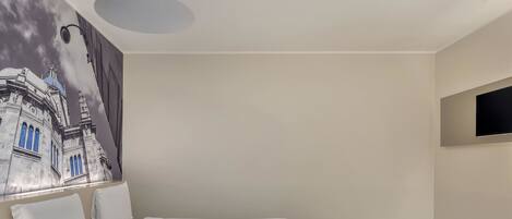 A hotel room with a bed, a desk, a chair, a TV, and a small table.
