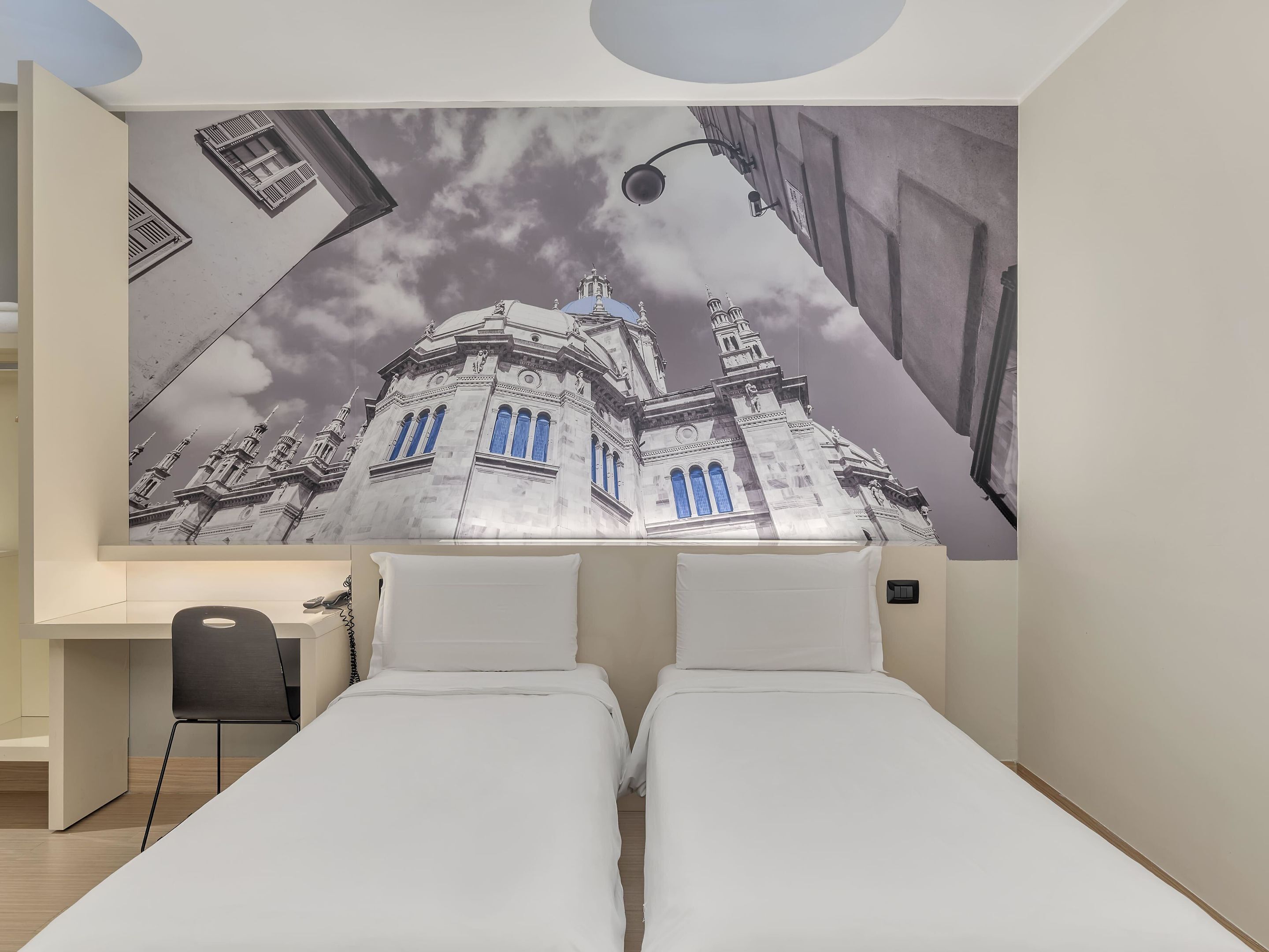 A bedroom with two beds, a desk, and a large wall mural of a building.