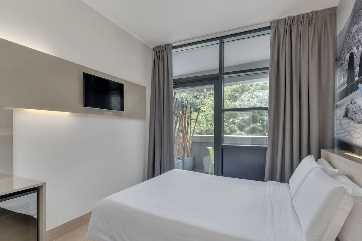 A modern hotel room with a bed, a TV mounted on the wall, and a window with curtains.