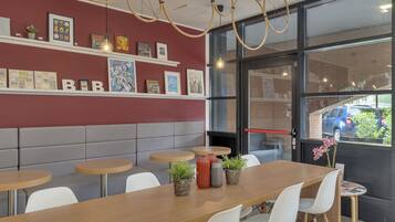 Ein modernes Café mit einem langen Holztisch, weißen Stühlen und einer roten Wand mit gerahmten Bildern.